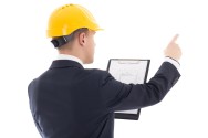 young handsome business man in yellow builder's helmet with blueprint pointing on something isolated on white background